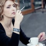 Девушка сидит в кафе с сигаретой и чашкой кофе