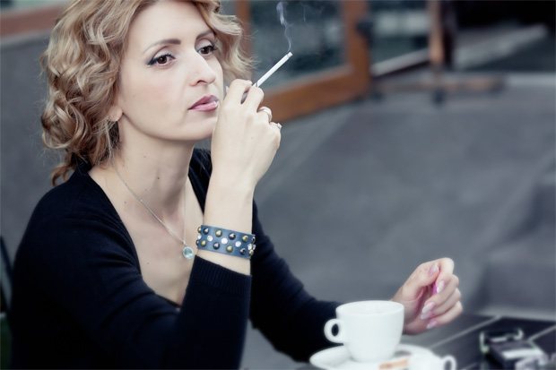 Девушка сидит в кафе с сигаретой и чашкой кофе
